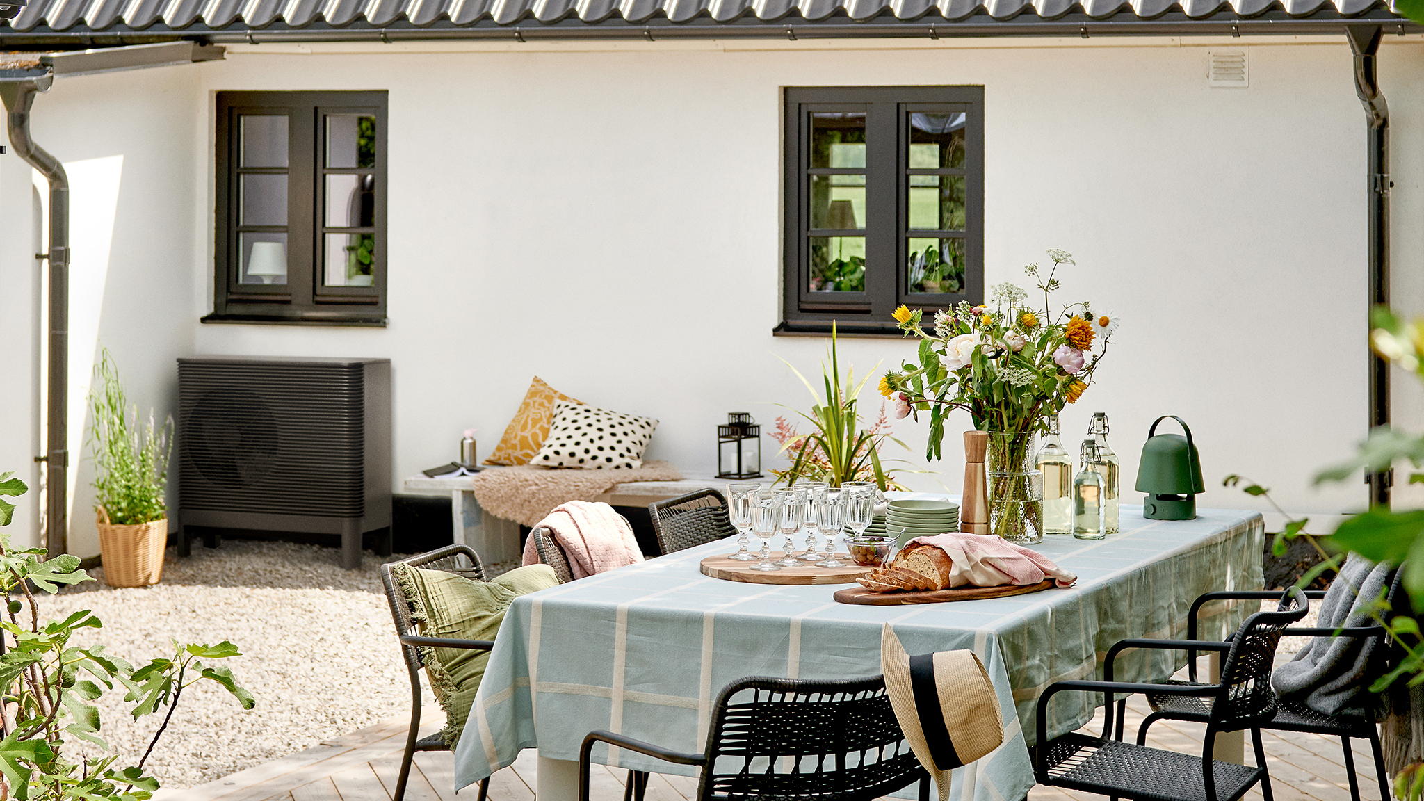 An IKEA x Aira air-to-water heat pump installed on a house with a dressed outdoor dining table next to it