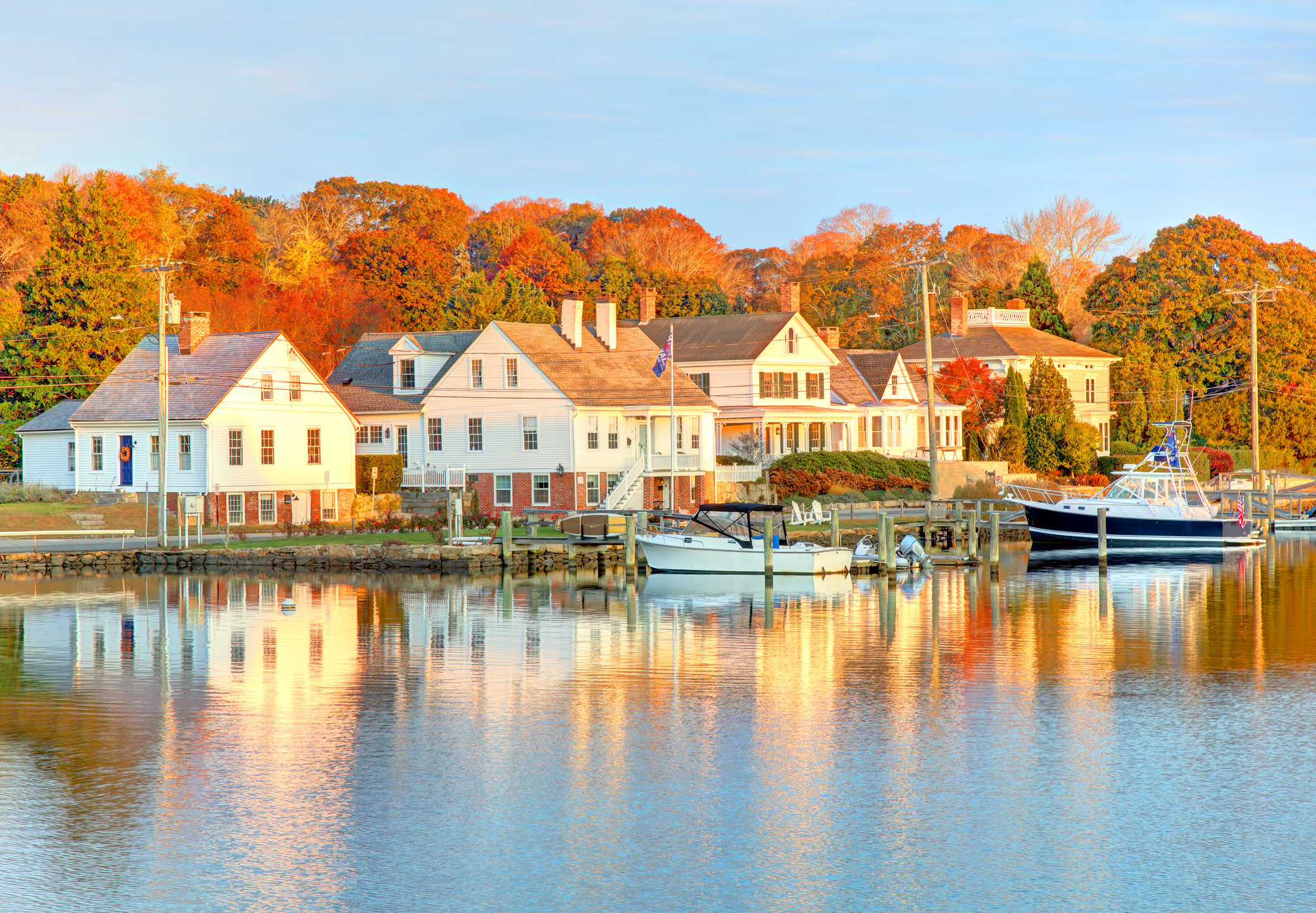 Various houses on a lake with boats in the water and autumnal trees in the background