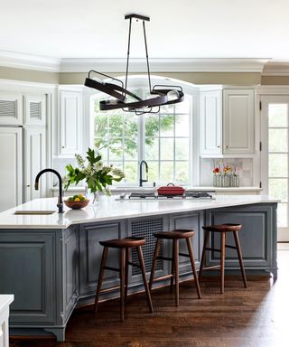 A kitchen with white walls, grey cabinets and triangular island with seating