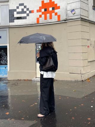 Eliza Huber trägt in Paris eine schwarze sportliche Jacke von Proenza Schouler mit einem weißen Popeline-Hemd, einer schwarzen Popeline-Hose und Flip-Flops.