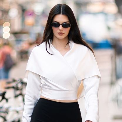 Kendall Jenner wears black capri pants with a white wrap top and a The Row bag in Paris.