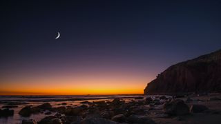a new moon at sunset over a rocky beach