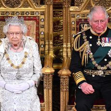 Queen Elizabeth and King Charles both wear ceremonial robes and sit on gold thrones