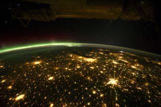 This photo shows several cities in the American Midwest at night as seen by an astronaut on the International Space Station on Sept. 29, 2011. The artificial light from human settlements appears with a characteristic yellow tinge. The green light of the aurora borealis also shines brightly in this view—even seeming to reflect off Earth's surface in Canada. Part of the ISS appears across the top of the image. \