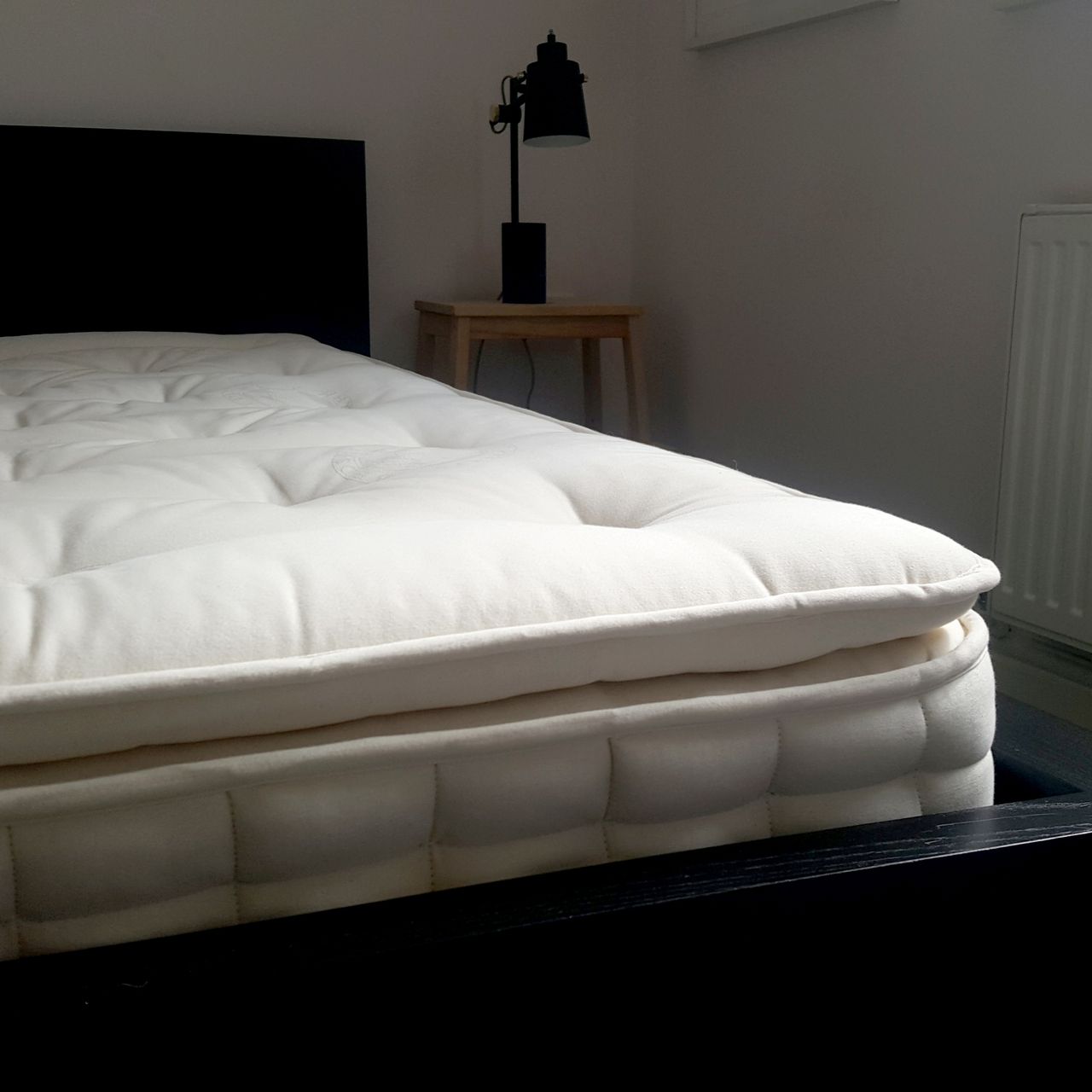 The Hypnos Pillow Top Classic mattress being tested in a bedroom with pale pink walls and a black bed