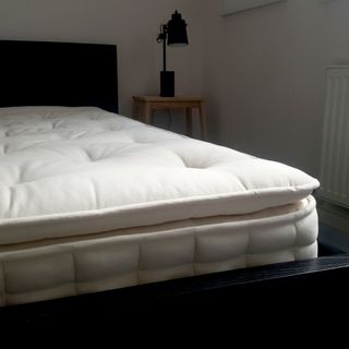 The Hypnos Select Pillow Top mattress being tested in a bedroom with pale pink walls and a black bed