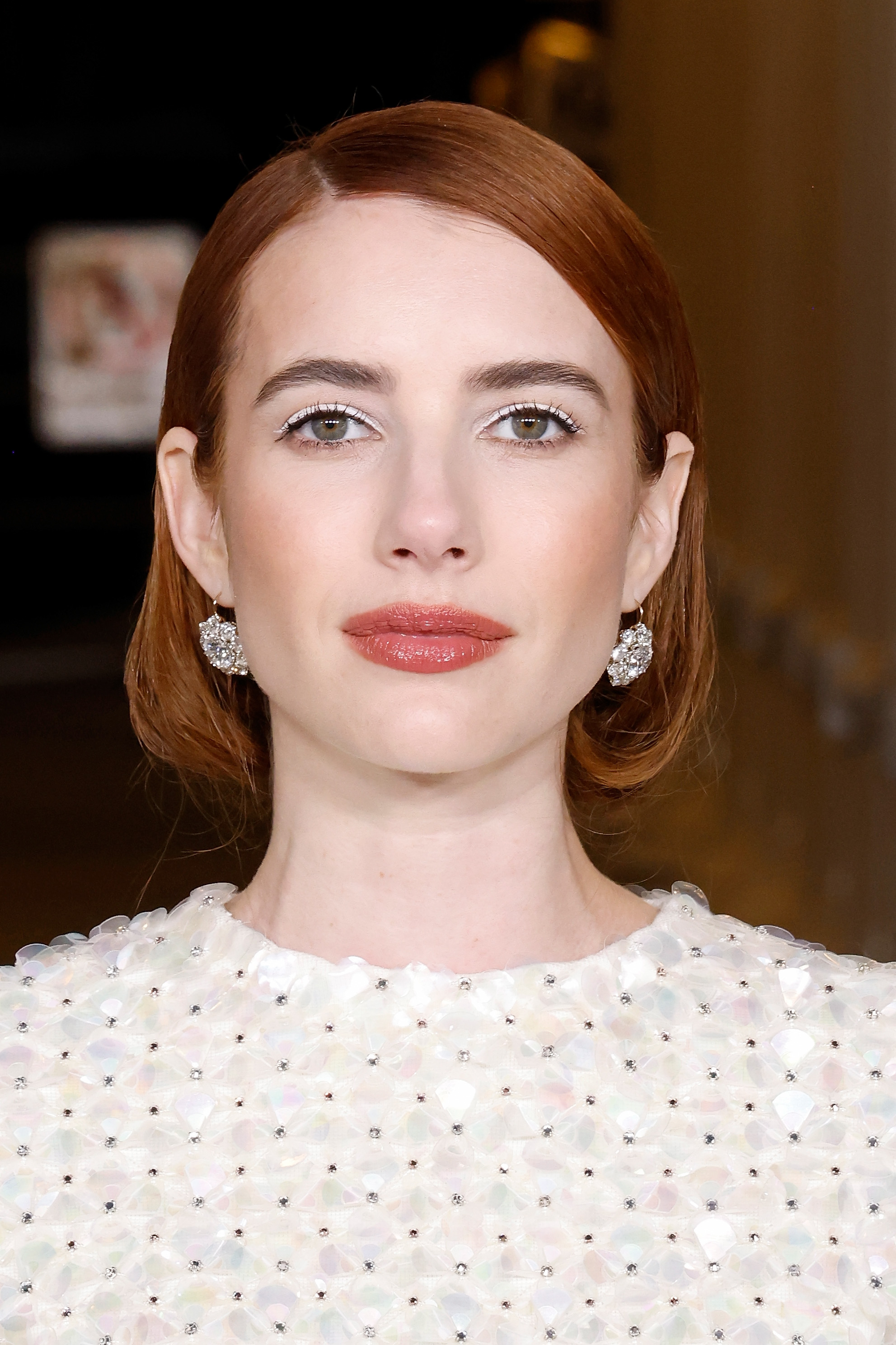 Emma Roberts with red hair, white eyeliner, a nude, rosy, lip and a white embellished dress