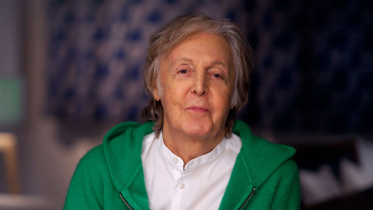 paul mccartney wearing a green sweater and a white shirt on a blue background