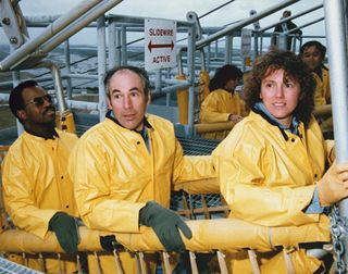 The STS-51L Challenger flight crew receives emergency egress training in the slide wire baskets. They are (L to R) Mission Specialist, Ronald McNair, Payload Specialist, Gregory Jarvis, Teacher in Space Participant, Christa McAuliffe. Directly behind them are Mission Specialist Judy Resnik and Mission Specialist, Ellison Onizuka.