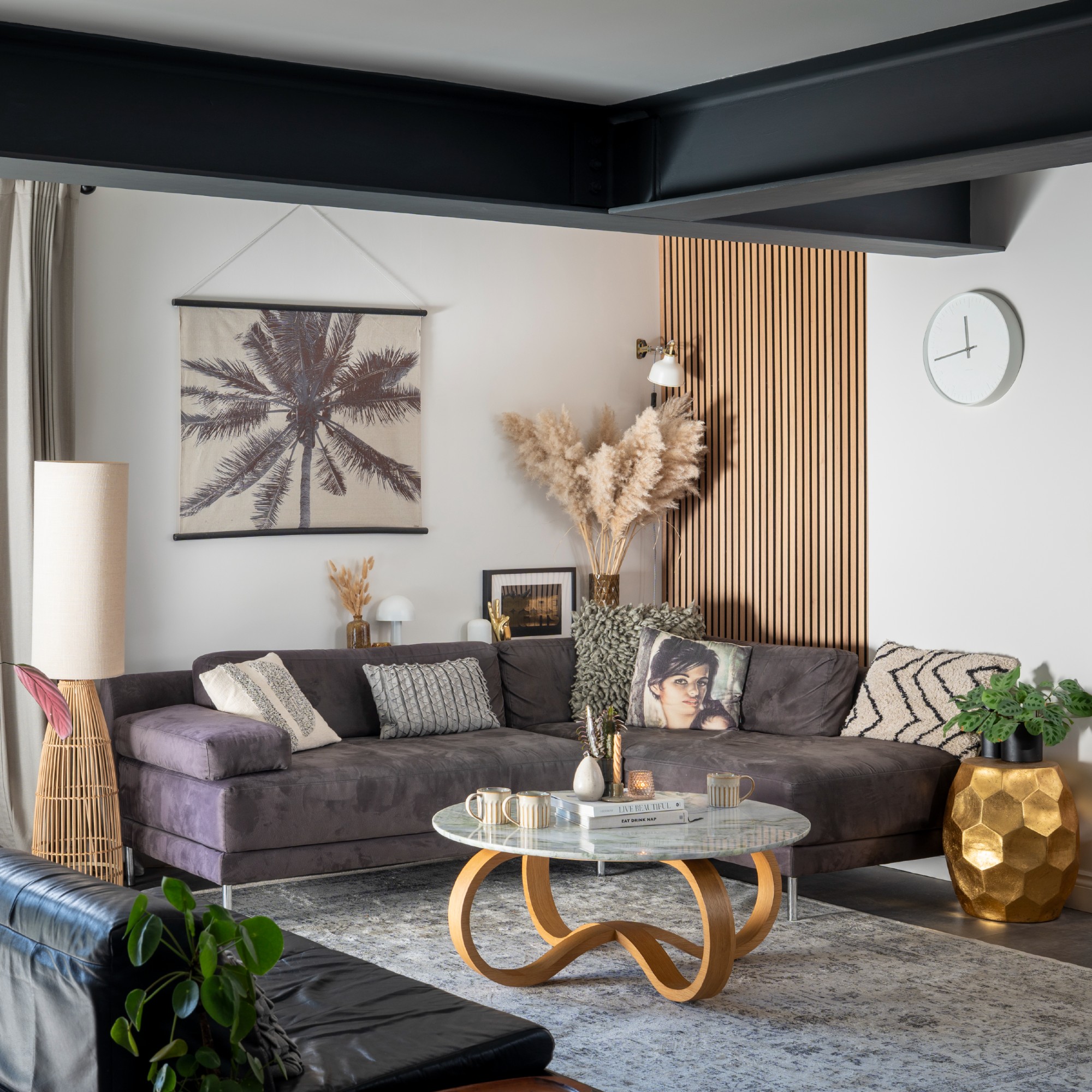 A white living room with a dark grey corner sofa with metal legs positioned in the corner with a round glass coffee table in front of it