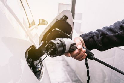 Detail of a hand plugging the cord into an electric car, to charge the battery in the garage outside a home. Concept of electric car charging, renewable energy, sustainability and transport.
