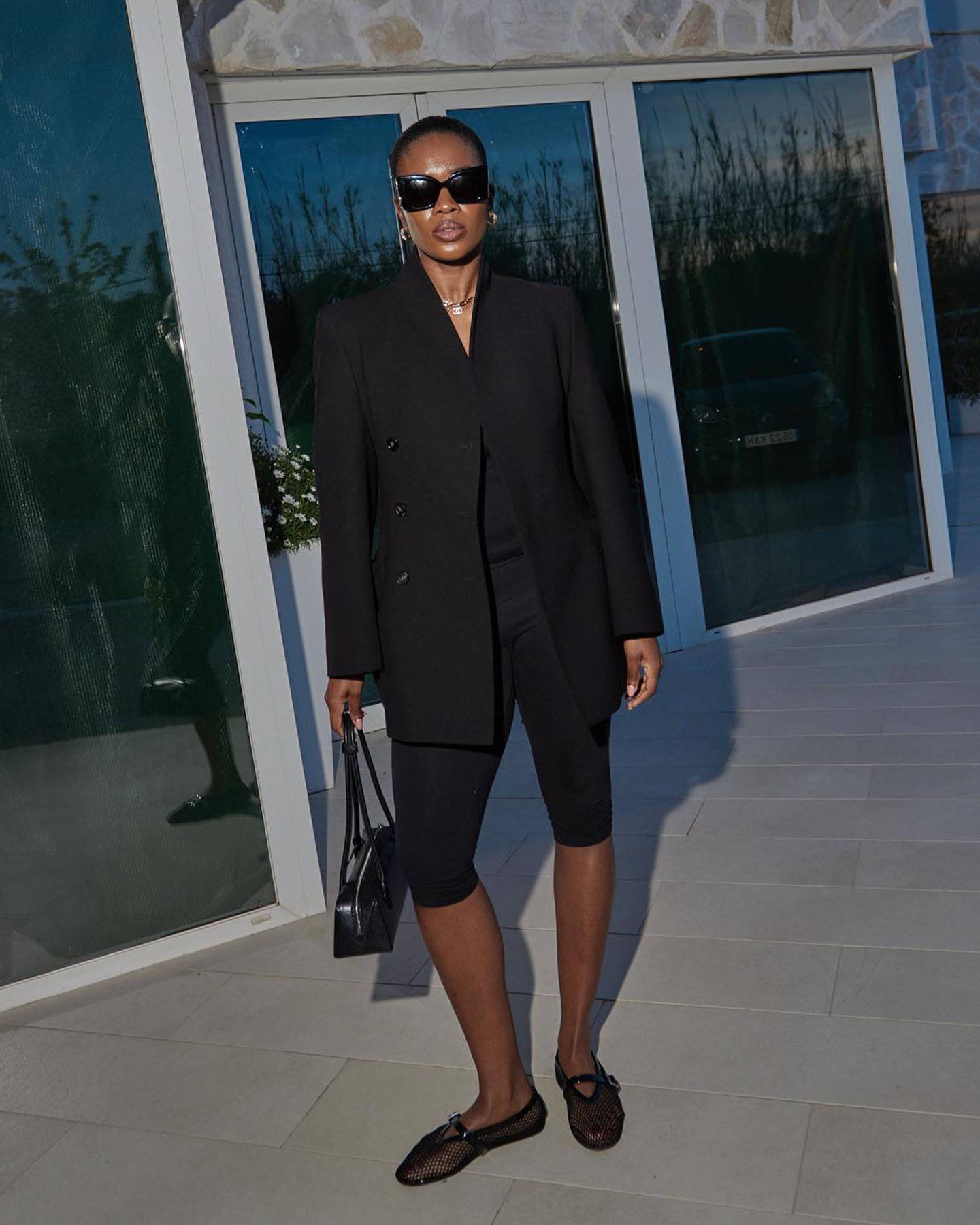 British influencer Marilyn Nwawulor Kazemaks poses in a black blazer, black top, black capri pants, an Alaïa bag, and mesh Alaïa flats