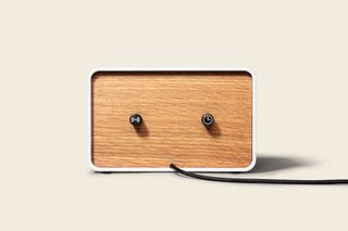 OneClock – a simple alarm clock with ‘waking music’. The back of a white rectangular clock with a wooden surface and two black dials on it.