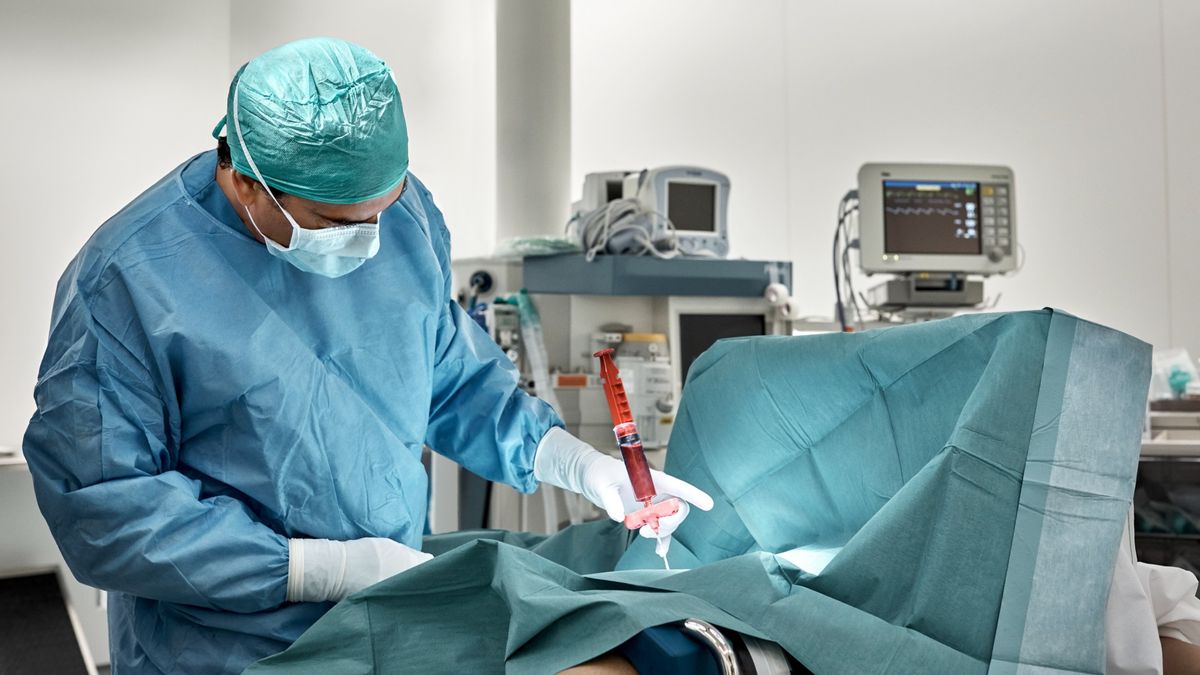 Surgeon monitors the extraction of bone marrow from a patient using a giant syringe in the operating theater