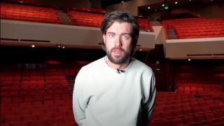 Jack Whitehall talking to camera in front of an empty venue in an announcement video for Jack Whitehall: Settle Down.