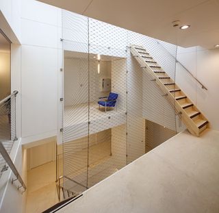 Interior view of the Super Cube featuring white walls, a blue chair, wooden stairs, handrails, mesh and a shaft in the centre