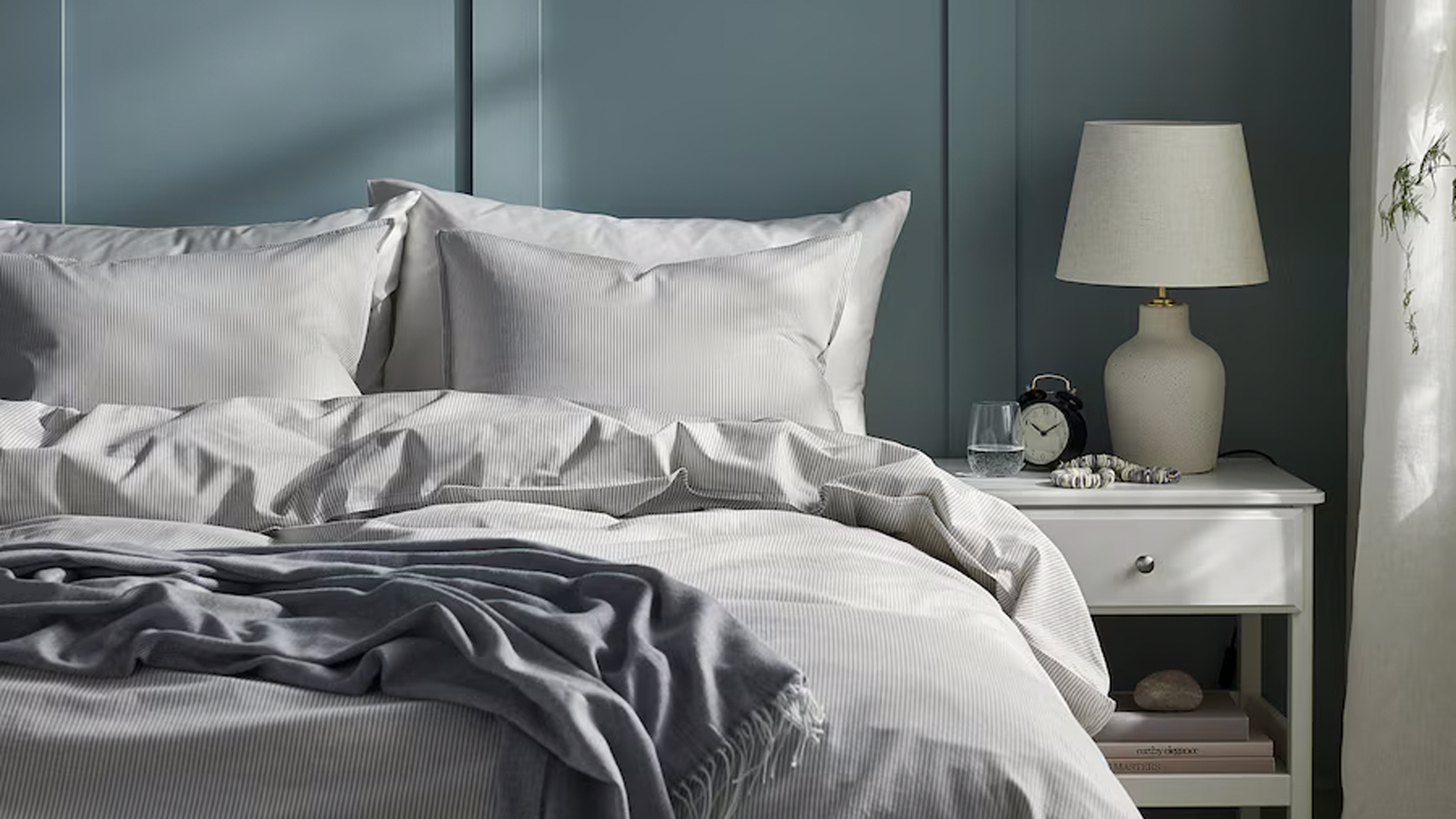 A bedroom with green panelling and a bed dressed in grey and white IKEA bedding