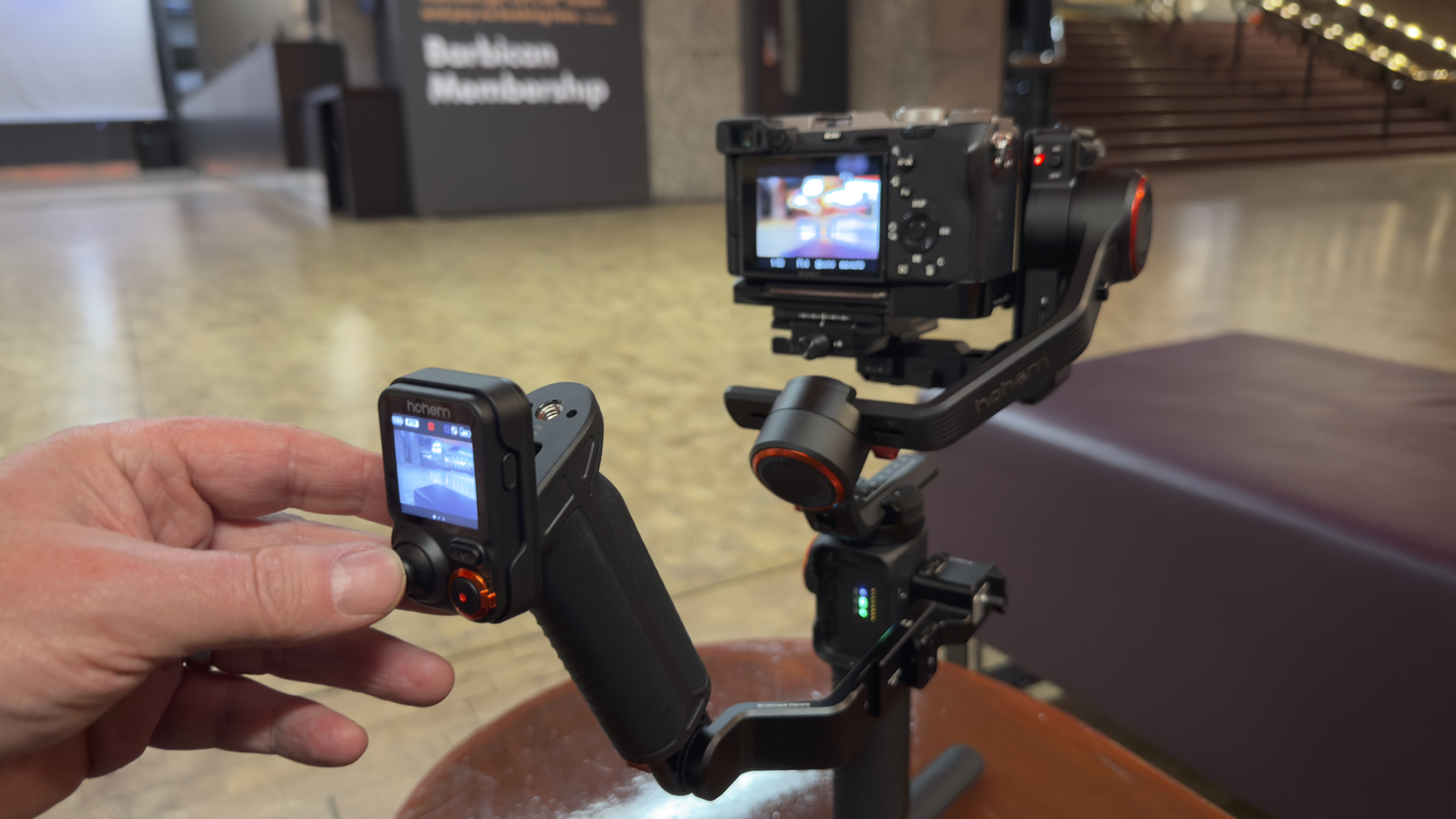 Hohem MT3 detachable remote controller held in hand beside the mounted camera and gimbal stabilizer.