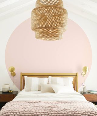 Blush painted large circle behind bed, with large rattan ceiling pendant, and chunky blush knit throw on bed.