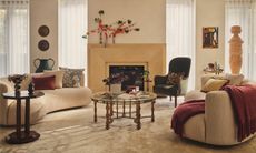 Warm neutral living room with curved sculptural sofas, layered textiles, vintage furniture and a central fireplace.