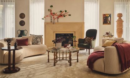 Warm neutral living room with curved sculptural sofas, layered textiles, vintage furniture and a central fireplace.
