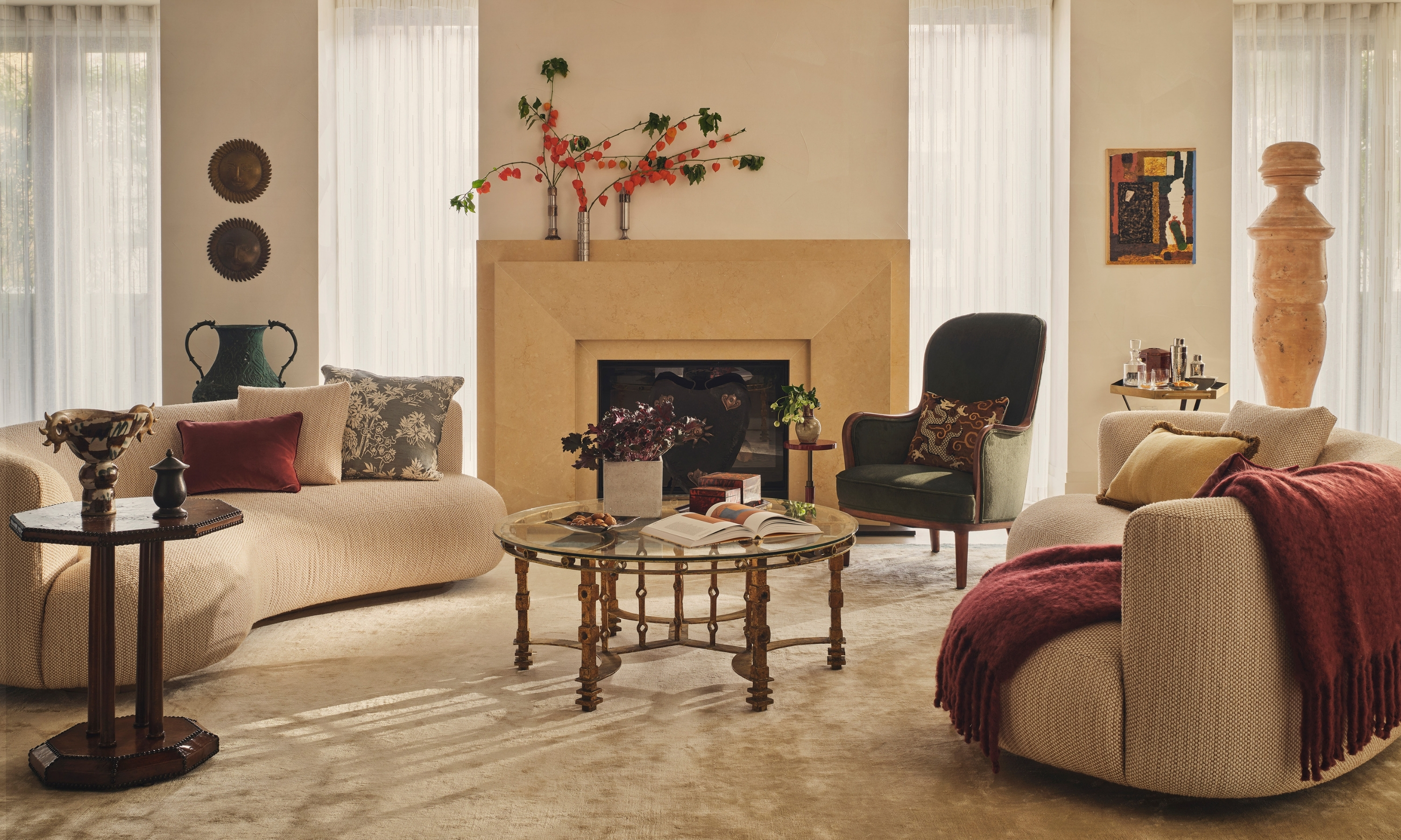 Warm neutral living room with curved sculptural sofas, layered textiles, vintage furniture and a central fireplace.