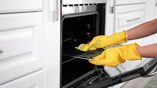 Someone cleaning an oven while wearing gloves