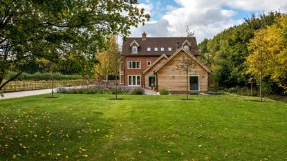 Exterior of a newly built house and outbuildings set in a newly planted and landscaped garden with a gravel drive.