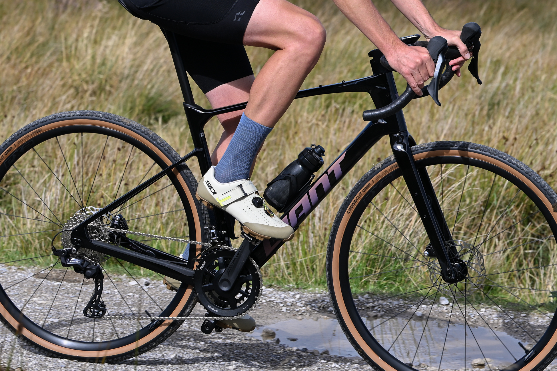 man riding a black gravel bike wearing black shorts, blue socks and beige SPD shoes