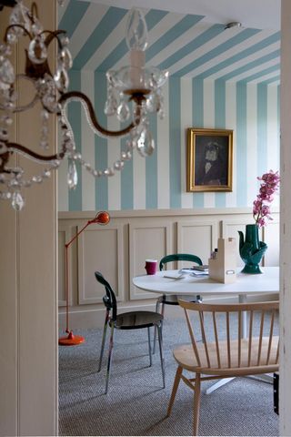 A dining room with cream wainscoting and blue and white striped walls