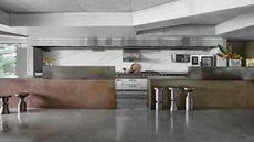 An industrial style kitchen with stainless steel worktops as well as metal stools beside the worktops and a metal features throughout different parts of the kitchen 