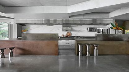 An industrial style kitchen with stainless steel worktops as well as metal stools beside the worktops and a metal features throughout different parts of the kitchen