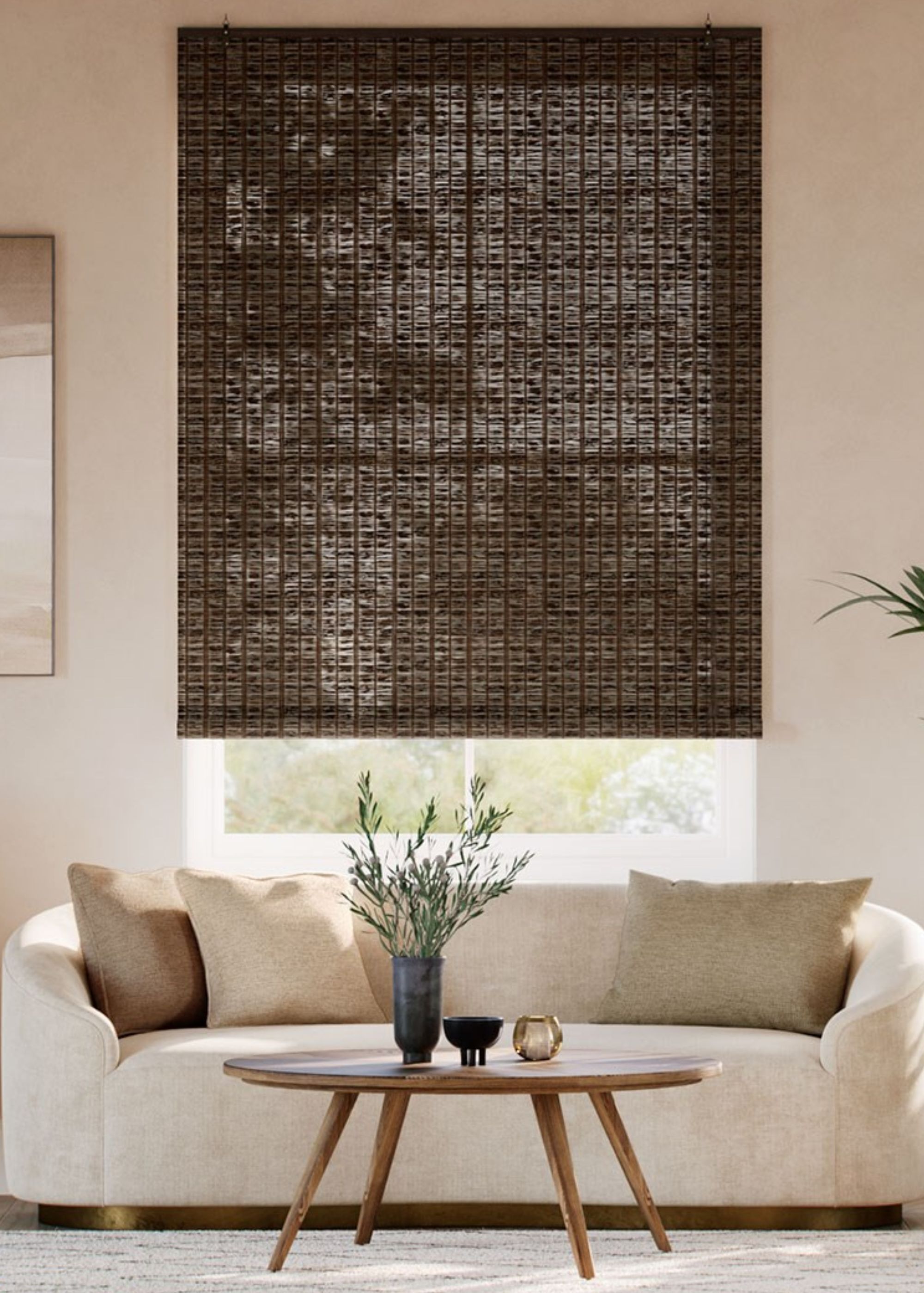 A walnut colored bamboo blind in a living room with a large sofa in front of the window. There is also a coffee table in front of the sofa with a plant and vase