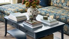 Two-tier navy blue coffee table with storage styled with stacks of coffee table books, a floral-patterned vase, match strike, and lit candles.