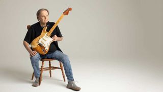 Walter Trout studio portrait, sitting on a chair holding a Stratocaster