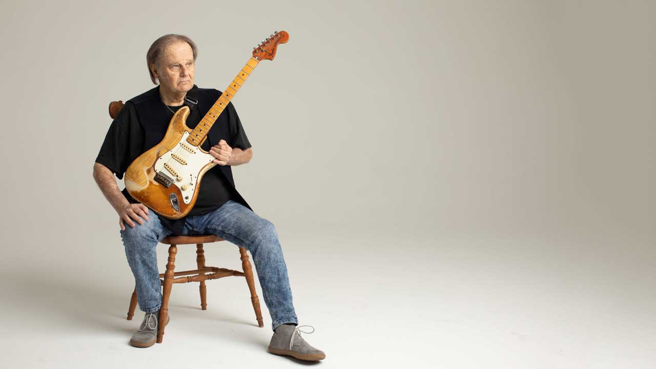 Walter Trout studio portrait, sitting on a chair holding a Stratocaster