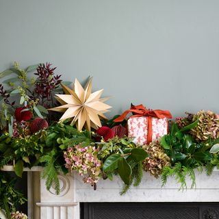 christmas flower arrangement draped over a white mantlepiece with a gold star and red and white present