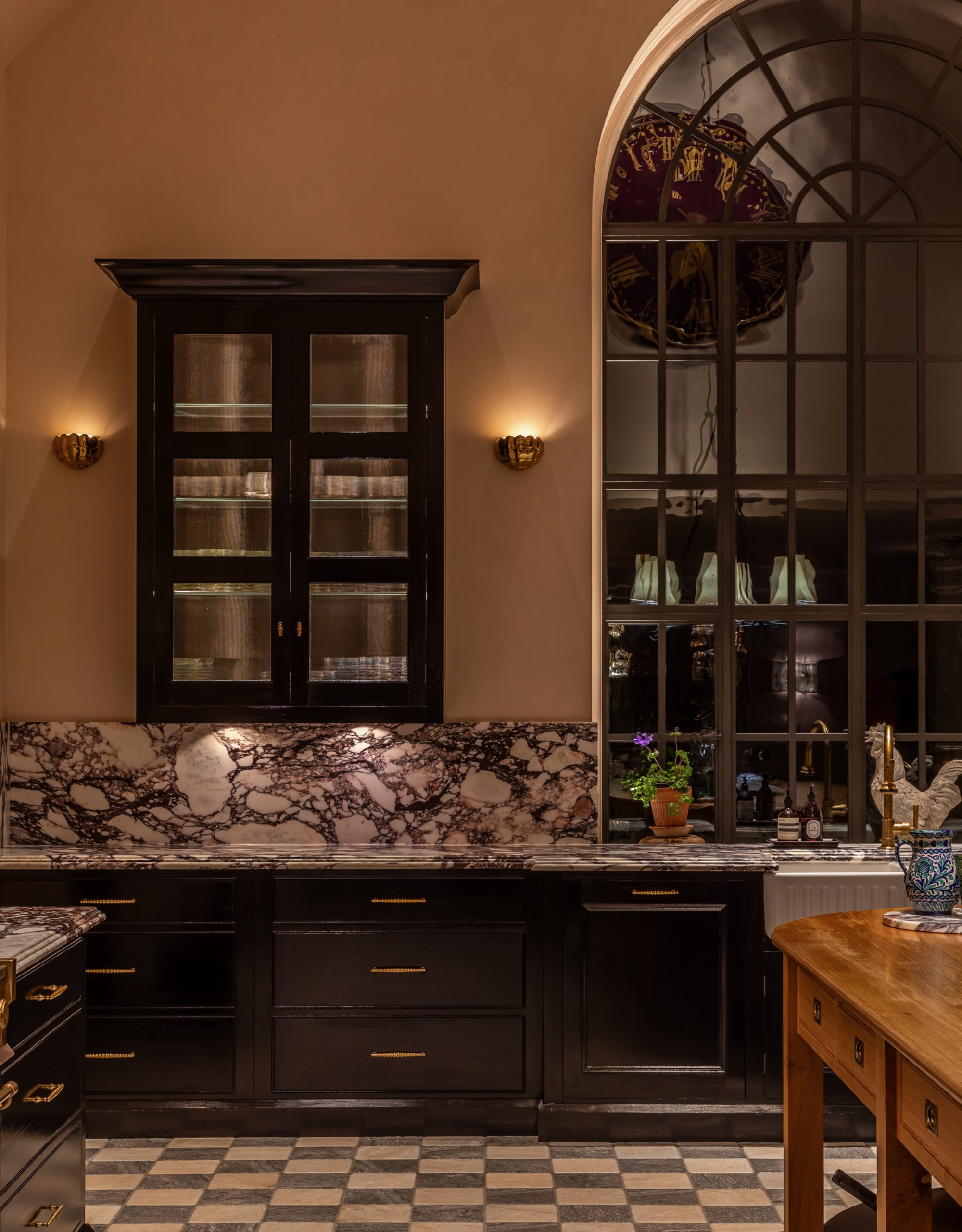 A country kitchen with large arched windows, checkerboard floors, and moody dim lighting