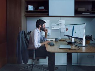 Man sitting on a desk with multiple computer monitors