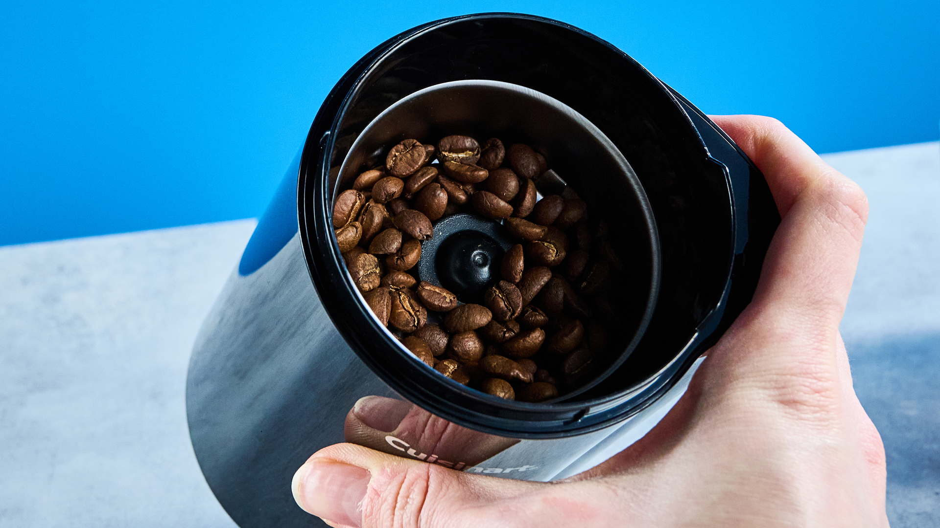 the cuisinart coffee grinder photographed against a blue background showing its blades and canister