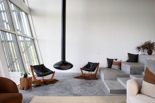 A modern seating area with cement flooring, leather stalls and a black metal stove suspended from the ceiling