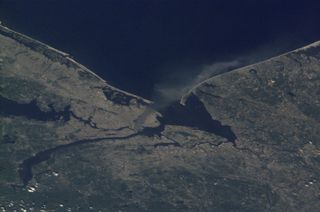 One of a series of pictures of metropolitan New York City taken by one of the Expedition Three crew members onboard the International Space Station (ISS) at various times during the day on September 11, 2001. A smoke plume rises from the Manhattan area where the World Trade Center was destroyed. The orbital outpost was flying at an altitude of approximately 250 miles.