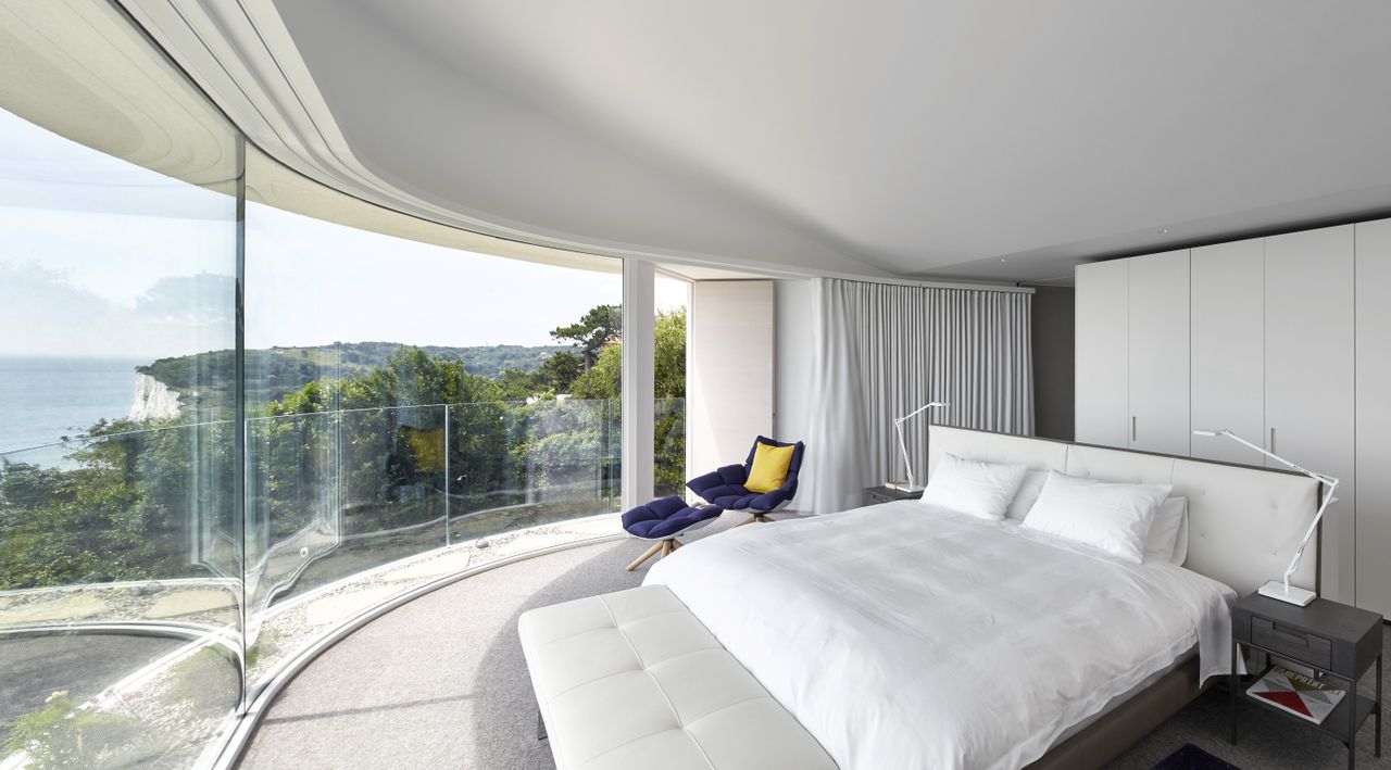 white bedroom with curved glazing and view to sea