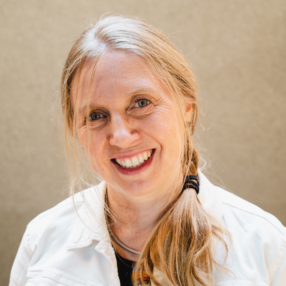 female with long blond hair in loose plait, smiling and wearing white shirt