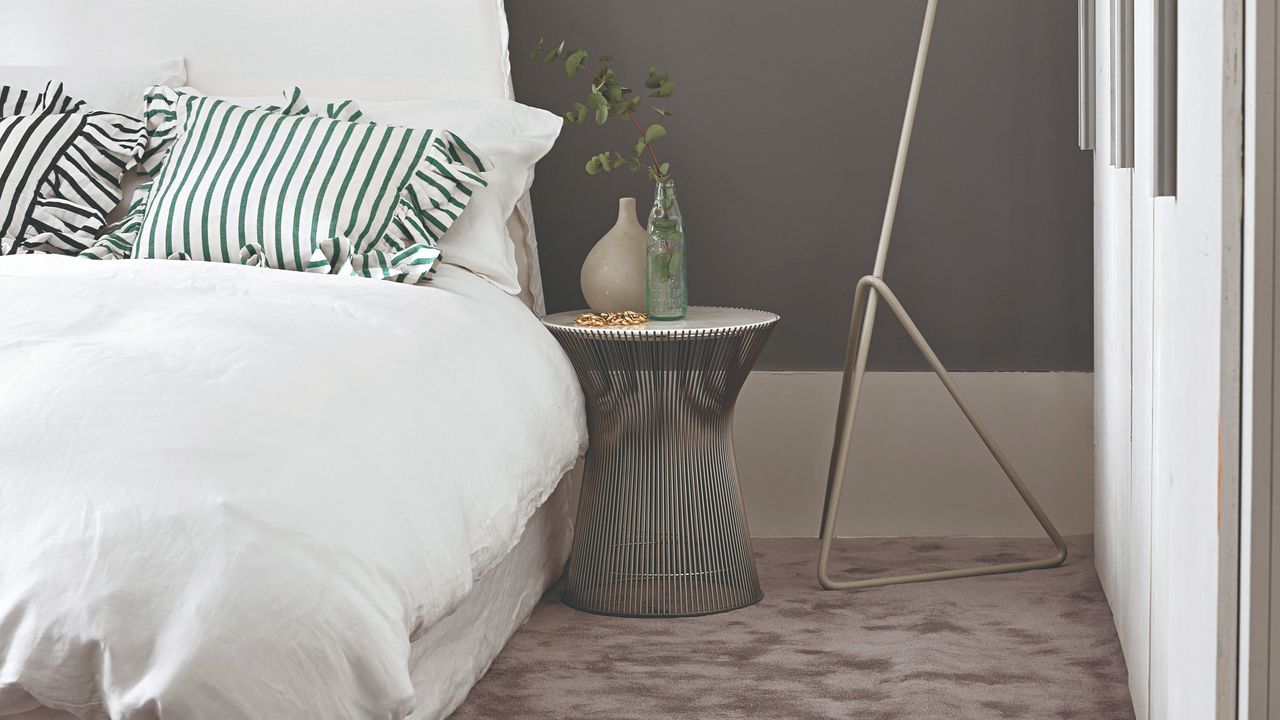 A bedroom with a grey fluffy carpet, white bedding and striped frilled cushions on top of the bed