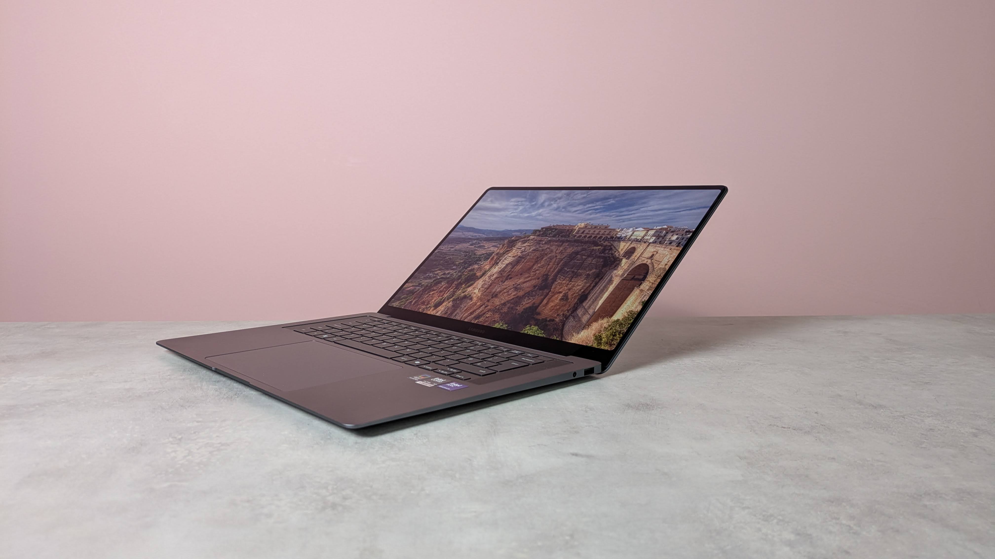 Three-quarter view of Samsung Galaxy Book6 Pro open on white desk with pink wall in background