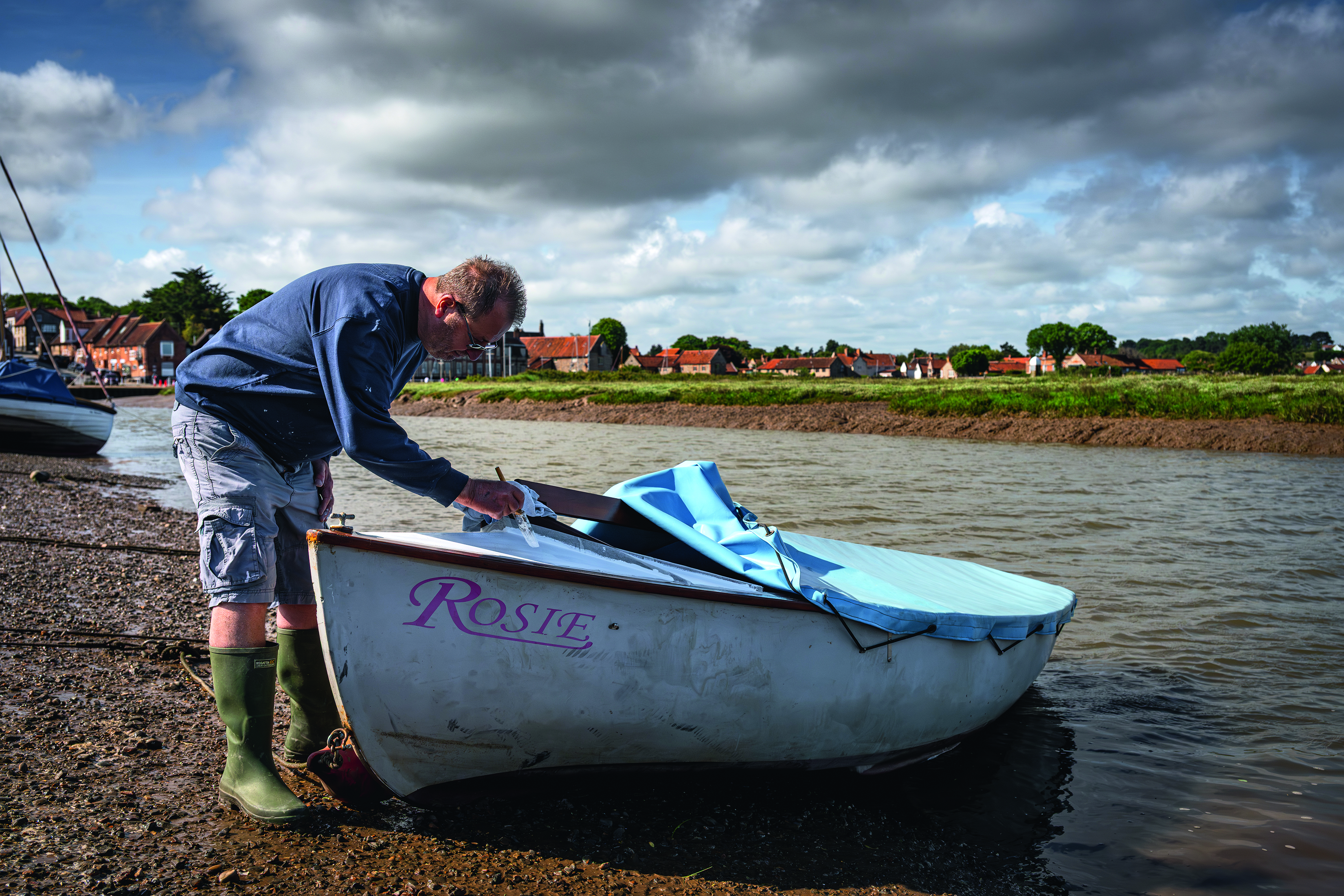 A man repairs his small boat, which is named Rosie, on the shore