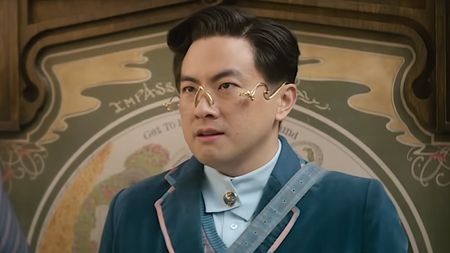 Bowen Yang wearing peculiar glasses and a school uniform in Wicked. 