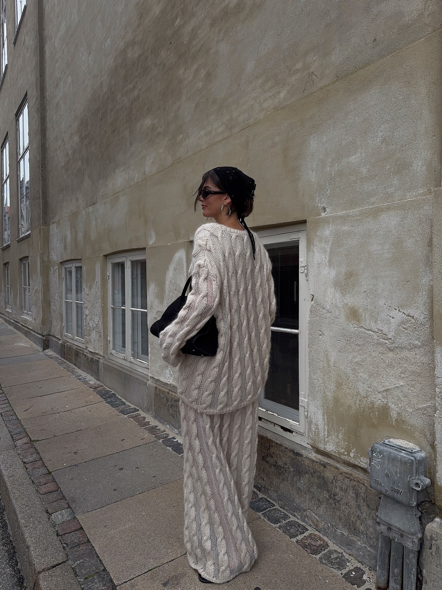 A woman wearing a head-to-toe cable knit long-sleeve sweater and sweater skirt.