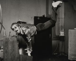 Photo of Elton John performing a handstand at a piano